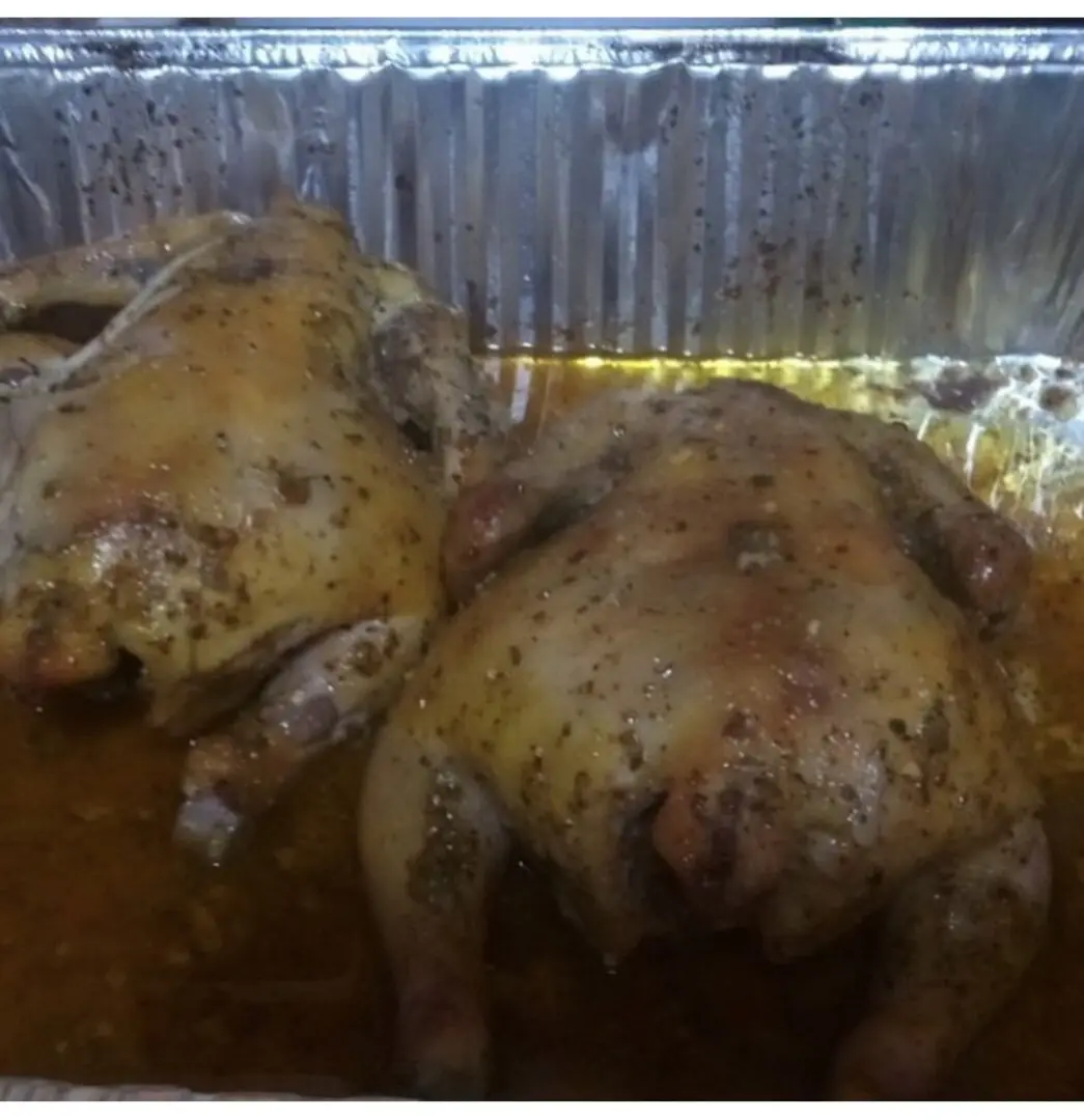 Two chickens are cooked in a tin foil pan.