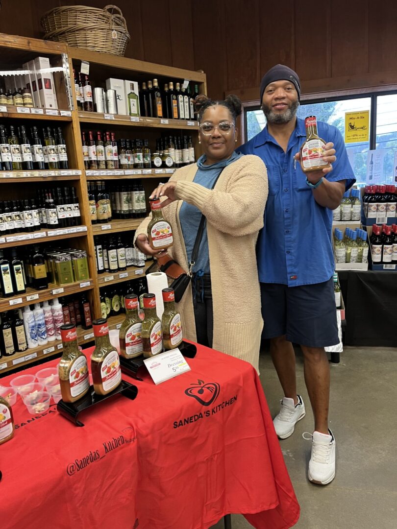 A man and woman holding up their hands in front of bottles.