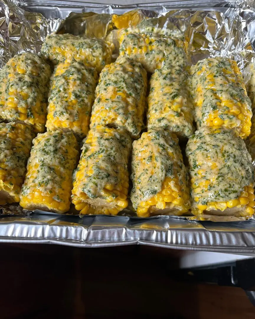 A tray of corn on the cob covered in cheese.